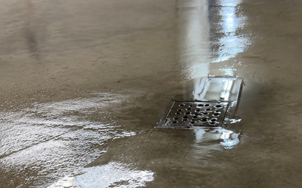 Même drain et plancher de béton après le rinçage à pression, avec la surface encore mouillée pendant l'évacuation de l'eau