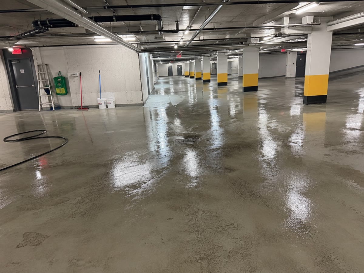 Vue large de la zone générale autour du drain, avec la dalle mouillée pendant l'intervention dans le garage souterrain à Montréal