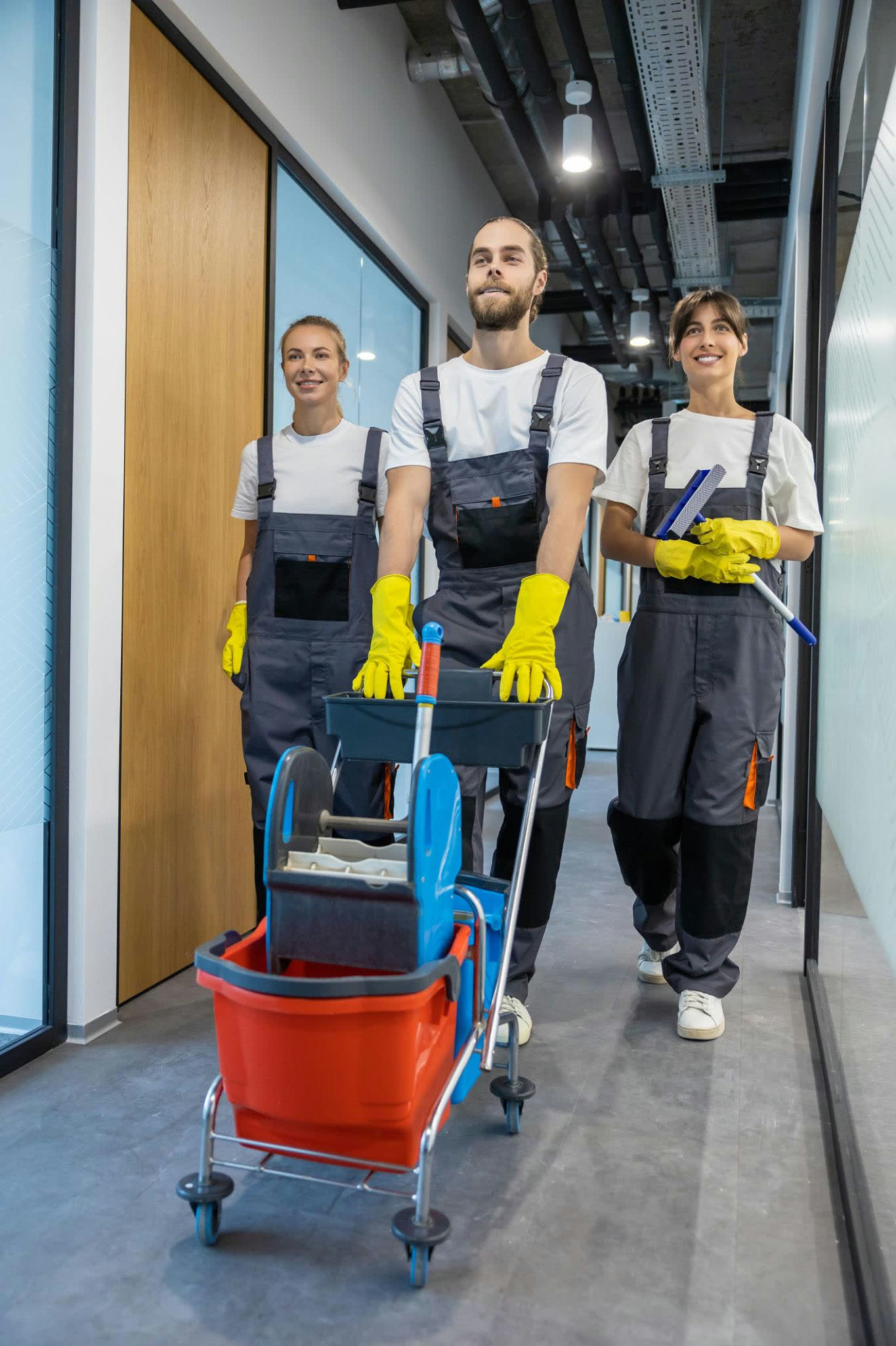 Three cleaning professionals moving through a commercial corridor with their equipment